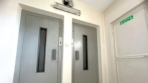 Deux portes d’ascenseur grises, avec un panneau de commande et un panneau de signalisation verte indiquant la sortie.