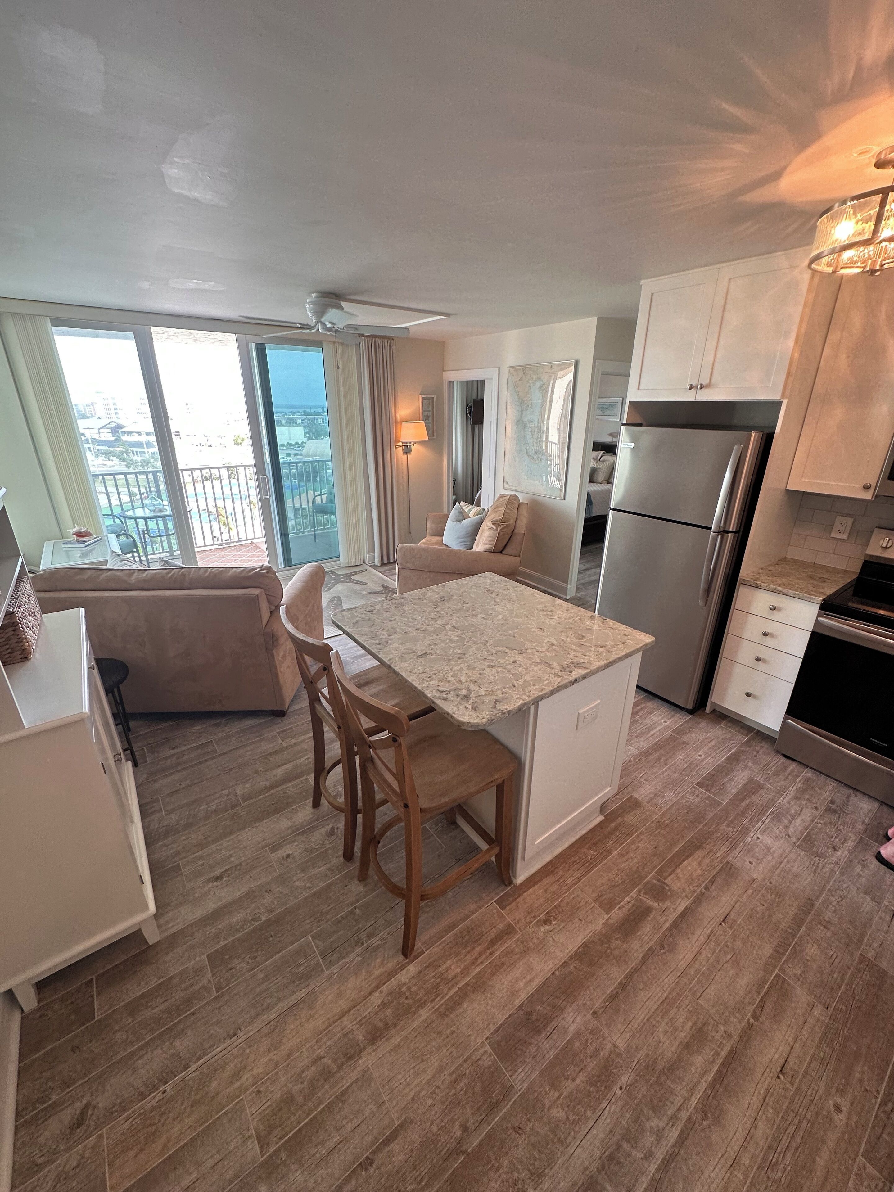 A modern kitchen with a central island, wooden chairs, a built-in refrigerator, and a view of the city through large windows.