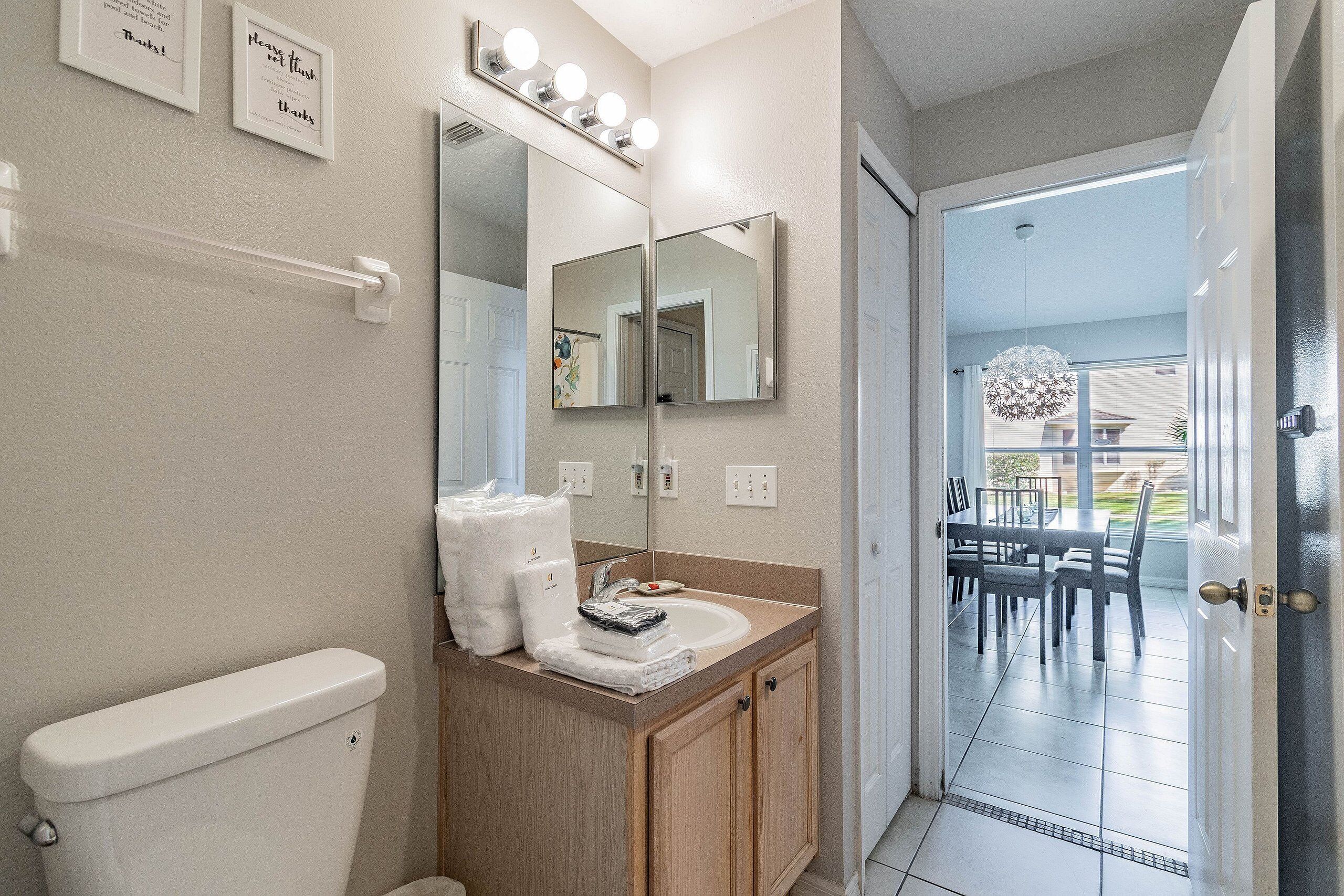 A bathroom with a toilet, sink, and mirror. There are towels and toiletries on the sink counter.