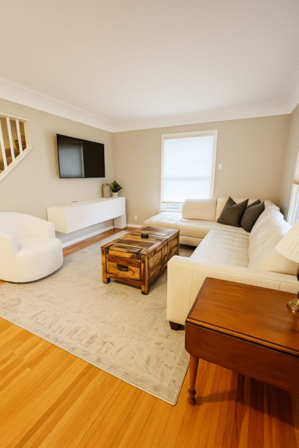 A modern living room with a white sofa, a wooden coffee table, and a TV mounted on the wall.