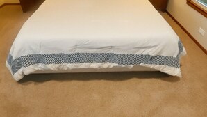 Un lit bien fait, avec une couette blanche et des taies d’oreiller à rayures, deux lampes de chevet et un coussin «détente» posé sur la tête de lit.