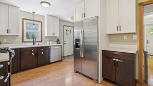 Une cuisine moderne avec des meubles blancs, un réfrigérateur en acier inoxydable et un plancher en bois.