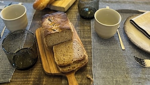 A wooden table with a loaf of bread, two cups, and a knife. - Le Mas des Poules chambres  (Saint-Roman-de-Malegarde)