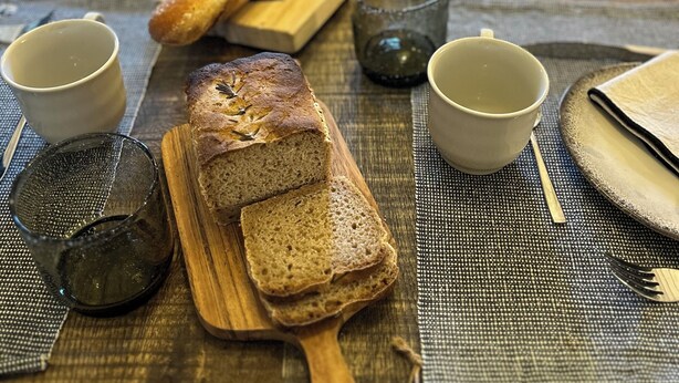 A wooden table with a loaf of bread, two cups, and a knife. - Le Mas des Poules chambres  (Saint-Roman-de-Malegarde)
