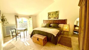 A bedroom with a bed, a chest of drawers, a desk, and a view of the outside. - Le Mas des Poules chambres  (Saint-Roman-de-Malegarde)