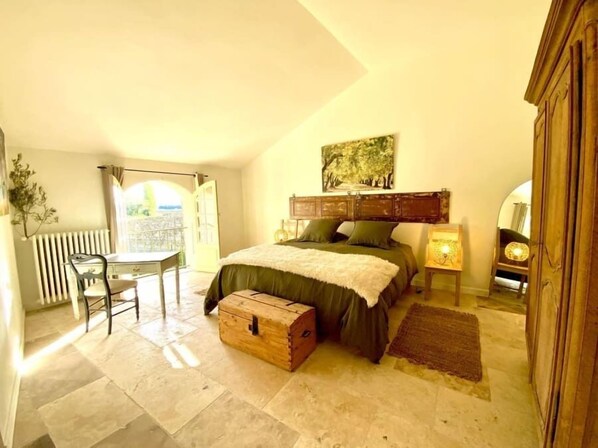 Ein Schlafzimmer mit Bett, Kommode, Schreibtisch und Blick ins Freie.