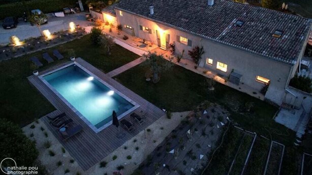 Una casa de dos pisos con piscina, mobiliario exterior y un patio bien iluminado.