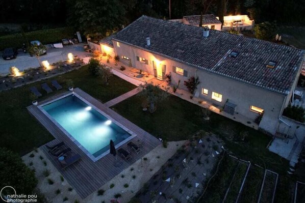 A two-story house with a swimming pool, outdoor seating, and a well-lit patio area. - Le Mas des Poules chambres  (Saint-Roman-de-Malegarde)