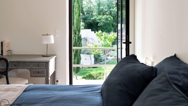 A bedroom with a bed, a desk, and a window with a view of a garden. - Le Mas des Poules chambres  (Saint-Roman-de-Malegarde)