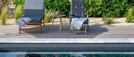 A poolside area with two lounge chairs, a small round table, and a hat on the table.