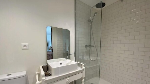 Un baño moderno con ducha de vidrio, lavamanos blanco y espejo.