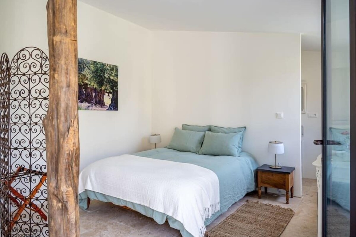 Un dormitorio con una cama, una mesita de noche, una lámpara, un cuadro y una estructura de madera.