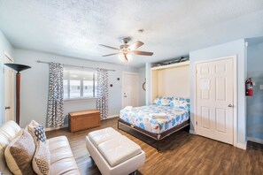 A bedroom with a bed, a sofa, a bench, a ceiling fan, and a window with curtains.
