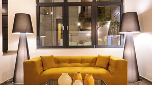 Una sala moderna con un sofá amarillo mostaza, una mesa de centro de vidrio y dos lámparas de pie.