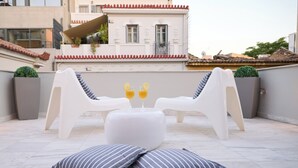 Una terraza en la azotea con dos sillones blancos, una mesa redonda pequeña y dos cojines a rayas.