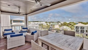 A covered outdoor seating area with wicker furniture and a wooden table, overlooking a residential area with multiple houses. - ☀️Luxury-Gulf Views-Bikes-Rooftop Lounge & Golf Cart-Caspian Escape☀️ (Santa Rosa Beach)
