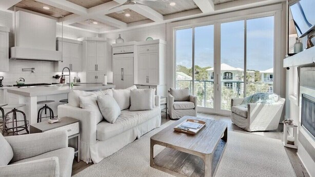 A modern kitchen with white cabinetry, a dining area with a white sofa and chairs, and a large window offering a view of a residential area. - ☀️Luxury-Gulf Views-Bikes-Rooftop Lounge & Golf Cart-Caspian Escape☀️ (Santa Rosa Beach)