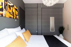 A modern bedroom with a large bed, striped wallpaper, a large mirror, and a ceiling light fixture. - Ma Maison Penthouse No1, Acropolis view, Huge terrace, 315 Mbps (Athens)
