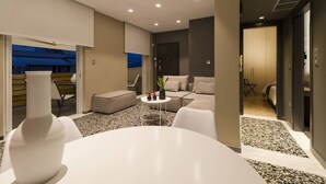 Une chambre d’hôtel moderne avec une table à manger ronde, un canapé et une petite table basse. Elle dispose d’un balcon avec vue sur la ville.