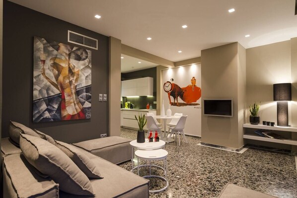 A modern living room with a large abstract painting, a sofa, a dining area with a table and chairs, and a kitchen in the background. - Ma Maison Penthouse No1, Acropolis view, Huge terrace, 315 Mbps (Athens)