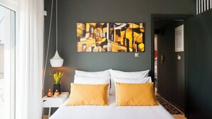 Une chambre d’hôtel moderne avec un grand lit, deux oreillers blancs, un oreiller décoratif jaune, une plante en pot et un tableau au mur.