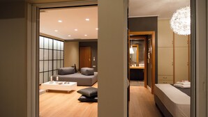 Une chambre d’hôtel moderne, équipée d’un canapé, d’une petite table, d’un lit et d’une salle de bain visible à travers une porte ouverte.