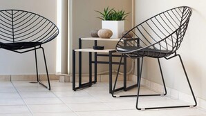 Un coin de pièce avec deux chaises en fil de fer noir, une petite table et une plante en pot.