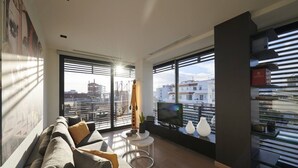 A modern living room with a large sofa, a TV, and a view of the city through large windows.
