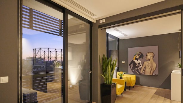 Un interno moderno con una porta scorrevole in vetro che dà su un balcone, un quadro di grandi dimensioni appeso al muro e una pianta in vaso.