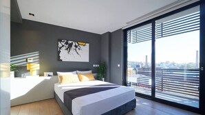Camera moderna con un letto grande, un comodino con una lampada, vista sulla città attraverso finestre a tutta altezza e un panorama urbano visibile all'esterno.