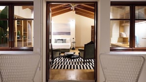 A hotel room with a bed, a desk, a chair, a black and white checkered rug, and a view through a doorway.