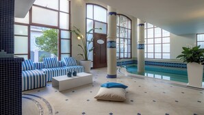A spacious indoor pool area with a sunlit seating area, large windows, and a pool with a tiled border. - Ma Maison N°8 Downtown Villa/Indoor Heated Pool (Athens)