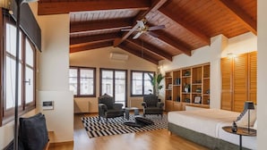 A spacious living room with wooden beams, a sofa, two armchairs, a coffee table, and a bookshelf.