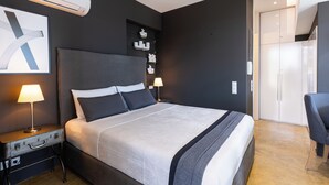 Une chambre d’hôtel moderne avec un grand lit, des lampes de chevet, une valise, une armoire et un téléviseur à écran plat.