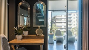 Un salon moderne avec un bureau en bois, deux plantes en pot, un haut-parleur rond et un grand miroir.