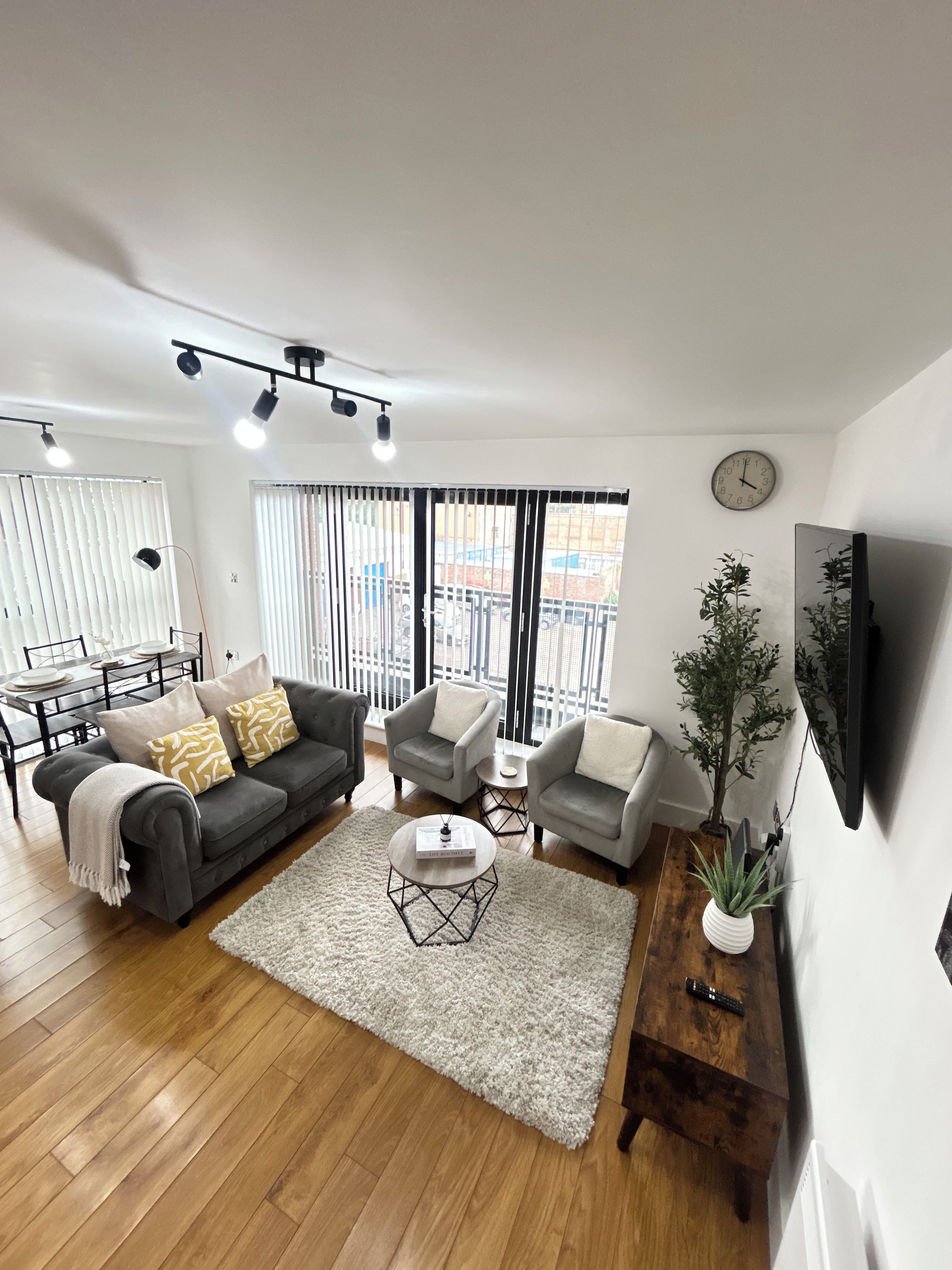 Una sala moderna con un sofá gris, dos sillones, una mesita de centro y un televisor montado en la pared.