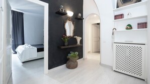 A modern hotel room with a black accent wall, a white bed, a vanity with a mirror and shelves, and a white radiator. - Babuino Luxury Design Apartment (Roma)