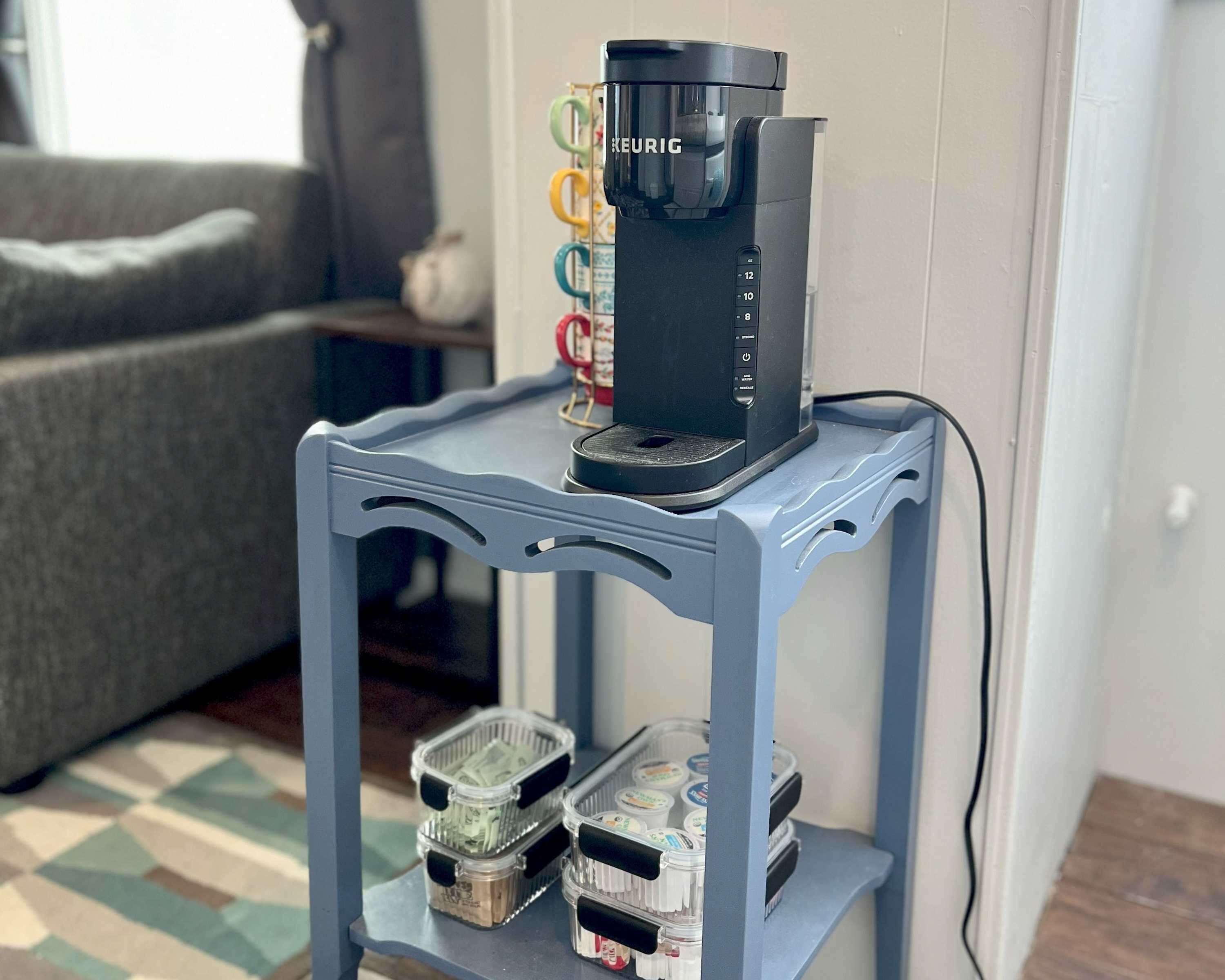 Une machine à café est posée sur une table bleue, et un plateau contenant divers récipients se trouve en dessous.