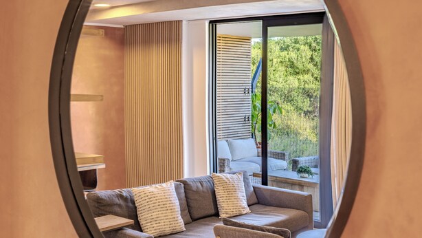 A modern living room with a sofa, pillows, and a view of an outdoor balcony.