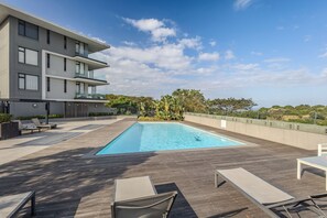 Un bâtiment moderne doté d’une piscine sur le toit, comprenant des chaises longues et offrant une vue sur un ciel d’un bleu éclatant.