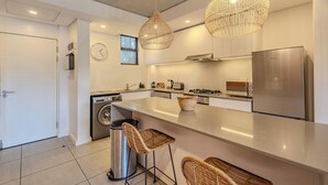 A modern kitchen with a large island, stainless steel appliances, and wicker bar stools.