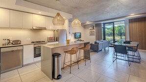 A modern kitchen with stainless steel appliances, a central island with bar stools, and a dining area with a glass table and chairs.