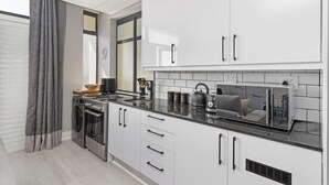 Een moderne keuken met witte kastjes, een inbouwoven, een magnetron en een waterkoker op het aanrecht.