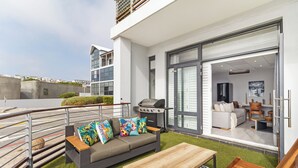 Een buitenruimte met een bank, een houten tafel en een barbecue.