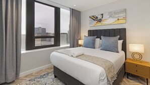 Quarto de hotel moderno com uma cama grande, vista da cidade pela janela e um quadro na parede.