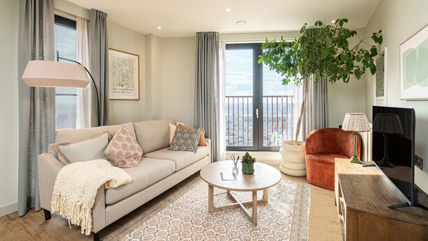 A modern living room with a sofa, a round coffee table, a red armchair, a TV, and a balcony with a plant. - The Eades ADC Atelier 2 Bed (London)