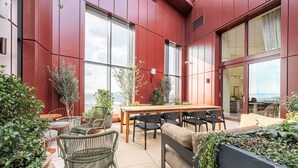 Uma área moderna para refeições ao ar livre, com mesa e cadeiras de madeira, cercada por plantas em vasos e vista para a cidade.