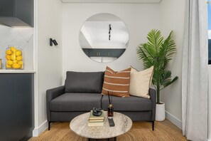 Una sala de estar moderna con un sofá gris, una mesa de centro redonda y un espejo grande en la pared.