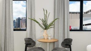 Habitación con vistas a edificios de la ciudad, una mesa redonda con una planta, dos sillas grises y un jarrón blanco.