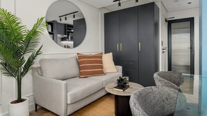 A modern living room with a grey sofa, a round mirror, a dark wardrobe, and a glass table. - Modern Studio in The Valour | De Waterkant Luxury (Cape Town)